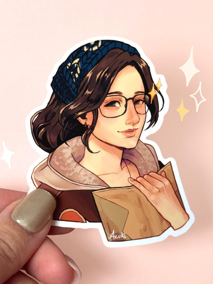 Die-cut vinyl sticker of Alma the Handler from Monster Hunter Wilds, brown wavy hair with a navy knit headband, glasses, a fur-collared coat, holding open her field-notes journal with a warm smile, held between fingers against a peach background.