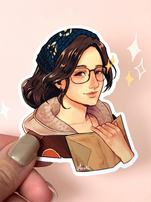 Die-cut vinyl sticker of Alma the Handler from Monster Hunter Wilds, brown wavy hair with a navy knit headband, glasses, a fur-collared coat, holding open her field-notes journal with a warm smile, held between fingers against a peach background.