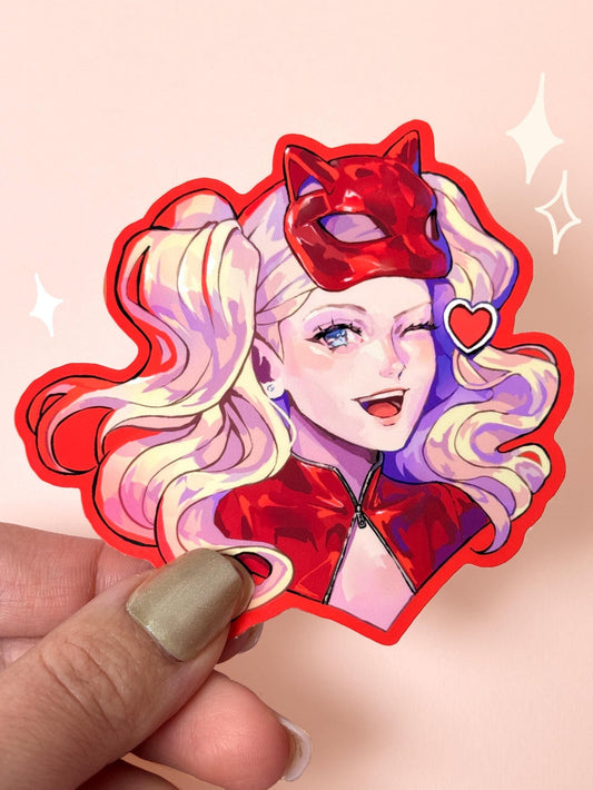 Die-cut vinyl sticker of Ann Takamaki (Panther) from Persona 5, winking and smiling in her red Phantom Thief catsuit and cat mask, held between fingers against a peach background.
