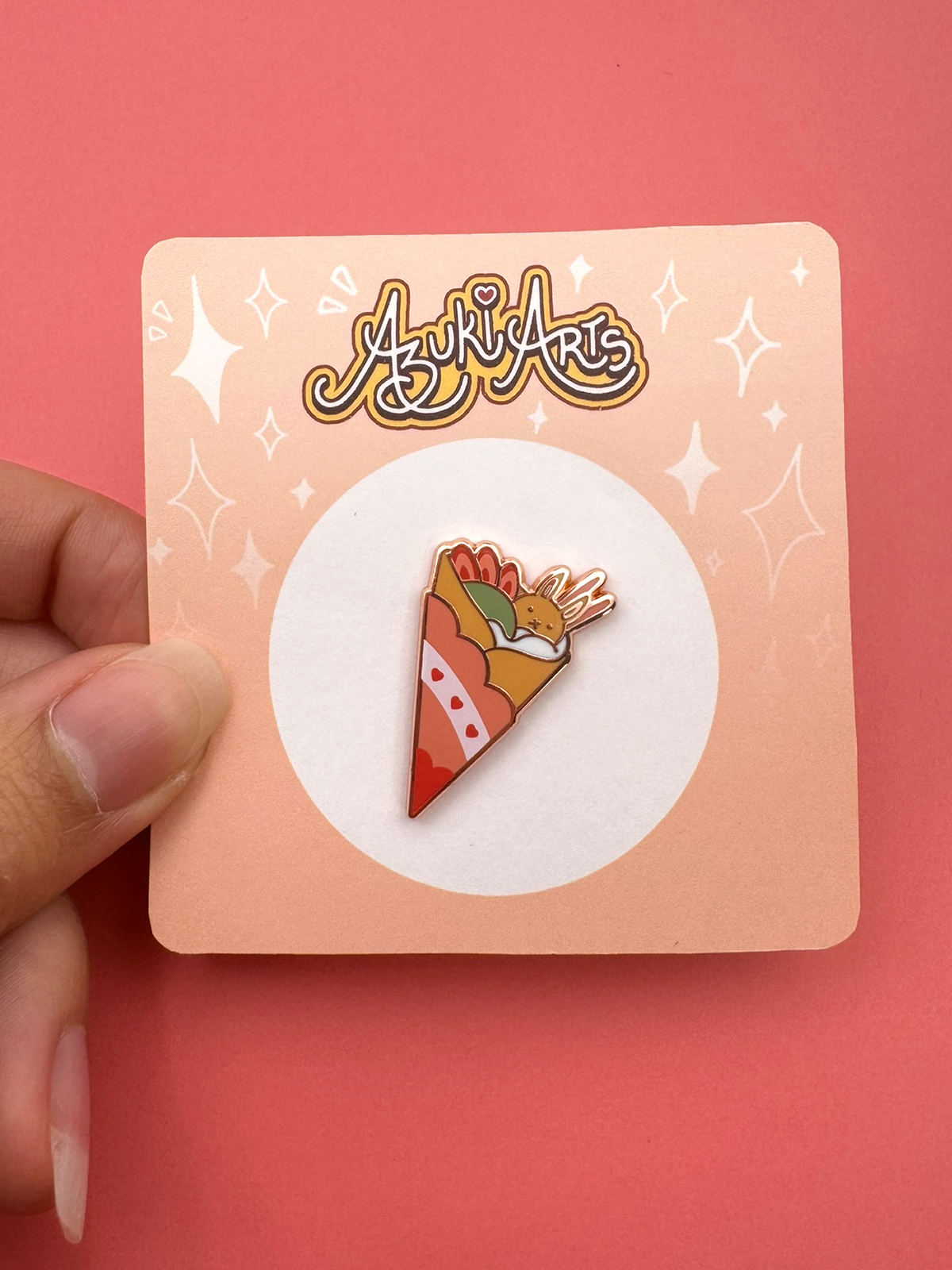 The bunny crepe enamel pin held in hand with packaging.