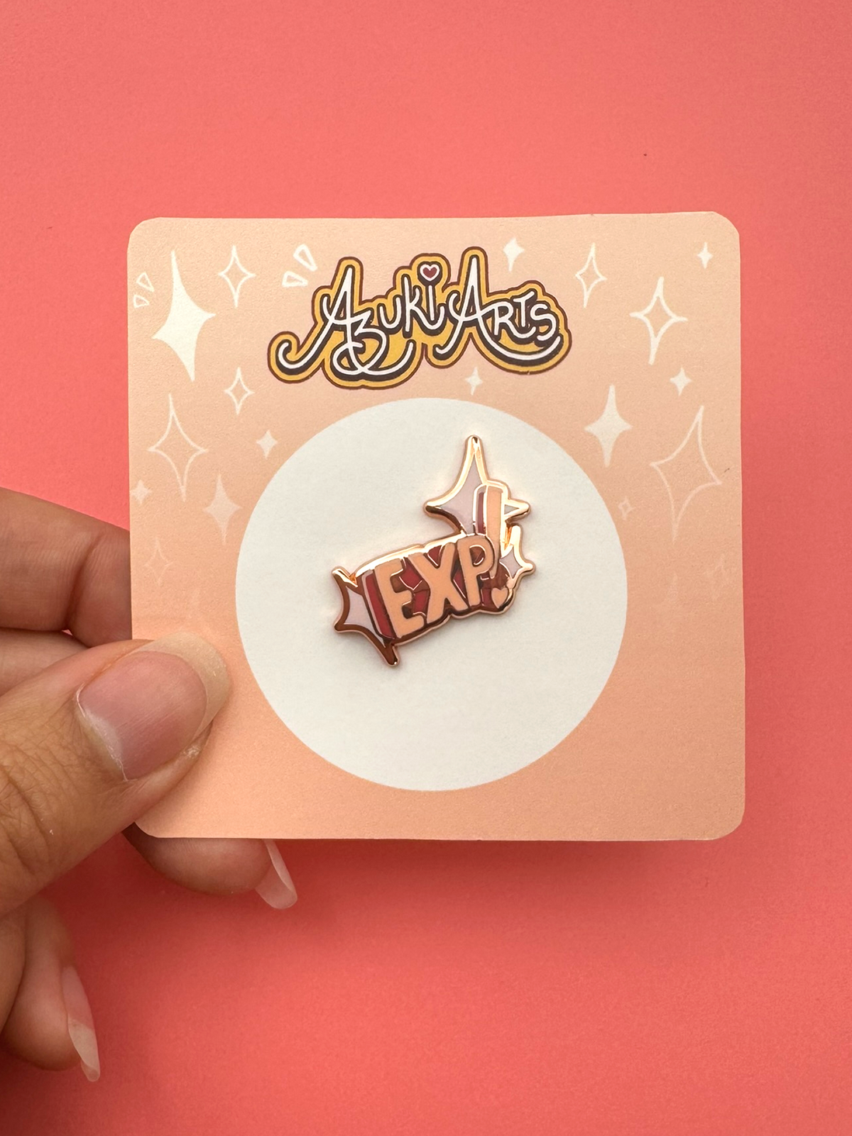 The large EXP enamel pin held in hand with its packaging.