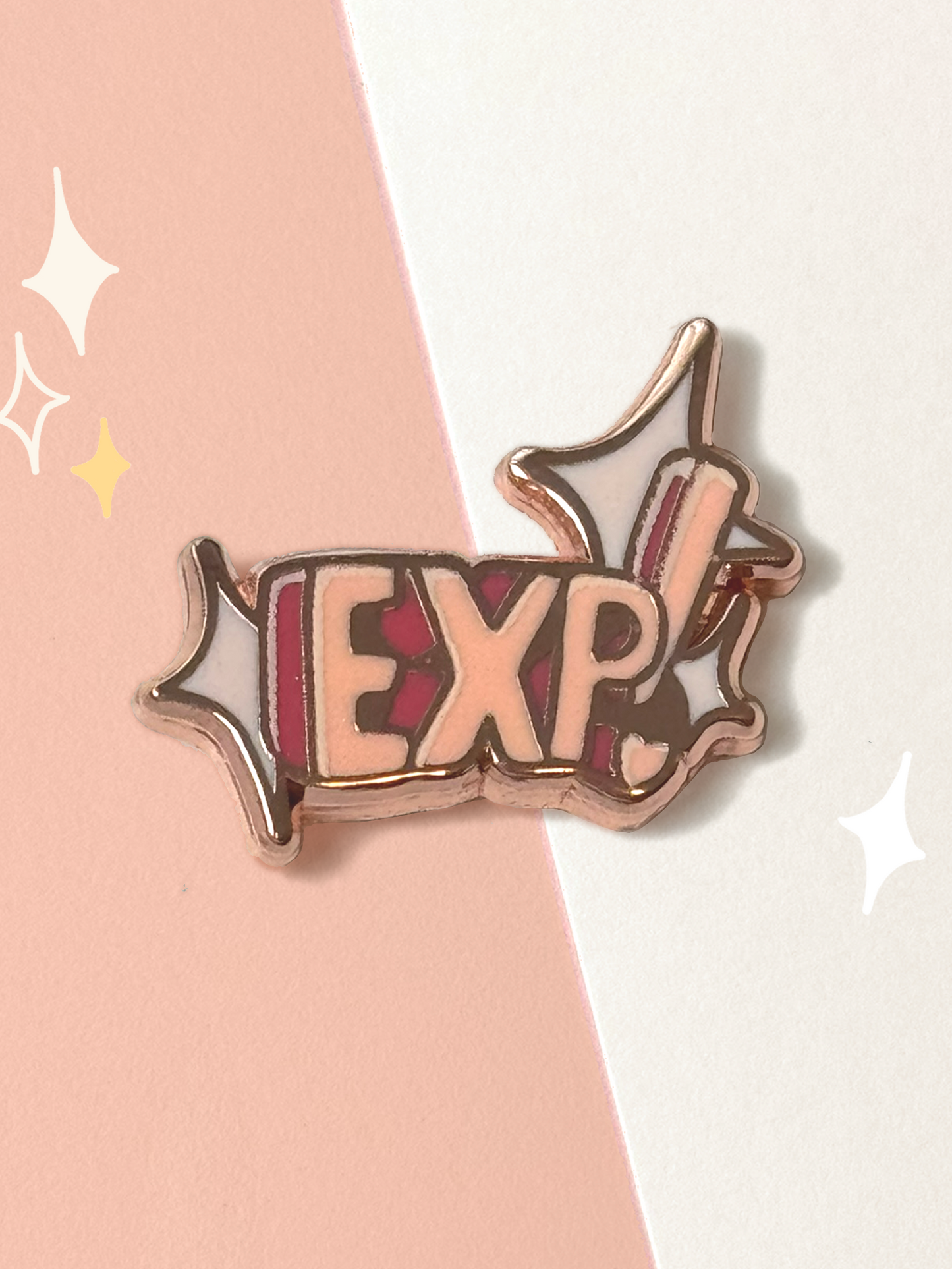 Hard enamel pin reading "EXP!" in peach block letters on a magenta banner with white sparkle bursts, outlined in rose-gold metal lines.