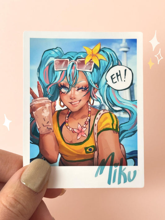 Polaroid-style vinyl sticker of Hatsune Miku in Brazilian gyaru style — turquoise twintails with pink streaks, yellow Brazilian-themed crop top, gold hoops, holding a Tim Hortons iced coffee in front of Toronto's CN Tower with an "EH!" speech bubble and "Miku" signature, held between fingers against a peach background.
