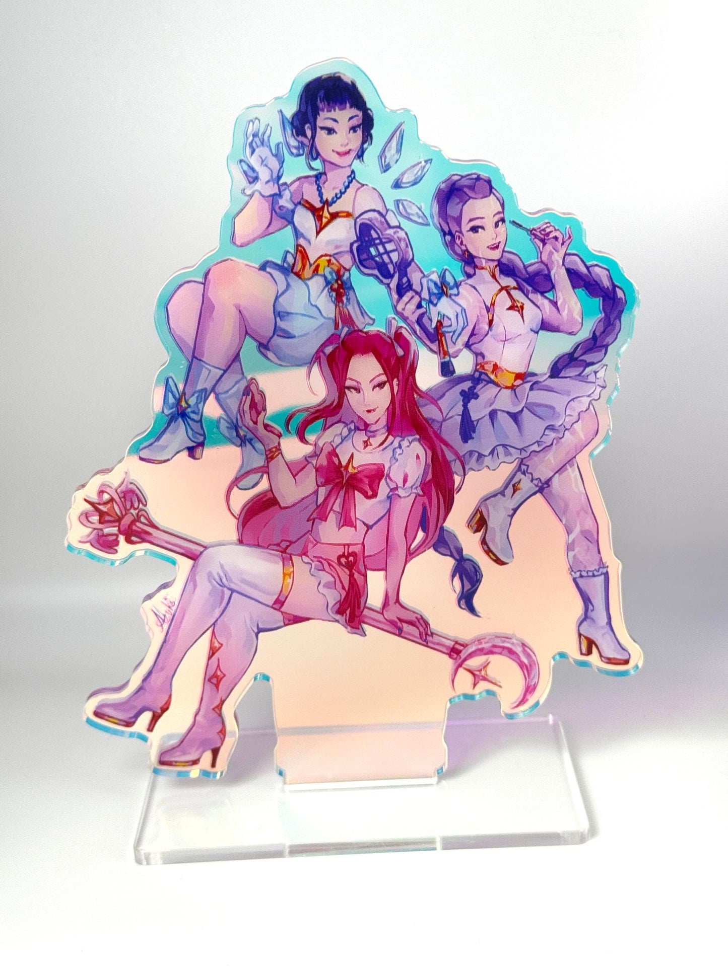 Rainbow iridescent acrylic standee of HUNTR/X from KPop Demon Hunters — Rumi, Mira, and Zoey in magical-girl outfits with their weapons, on a clear acrylic base.