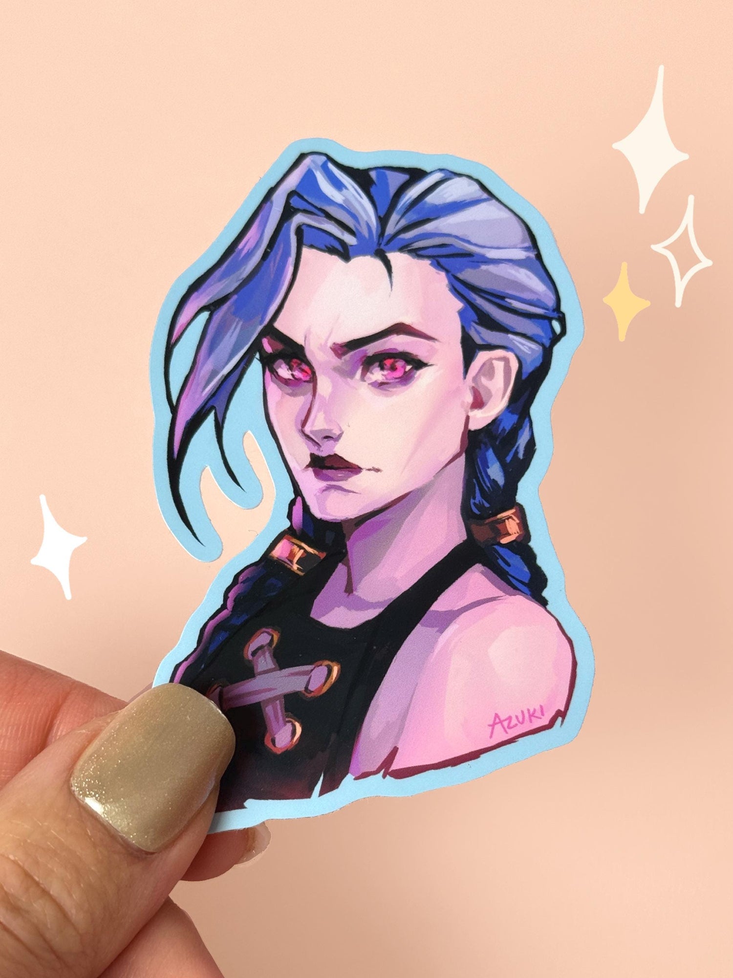 Die-cut vinyl sticker of Jinx from Arcane, with long blue braids, shimmer-pink eyes, dark lipstick and a powder blue border, held between fingers against a peach background.