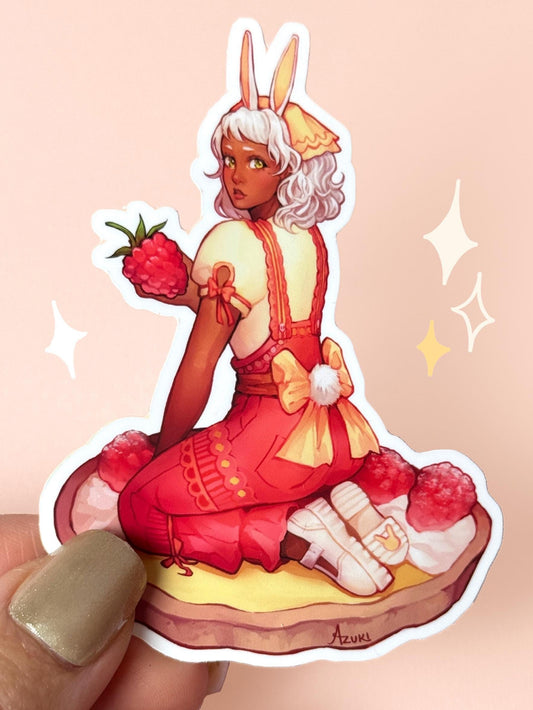 Die-cut vinyl sticker of a bunny girl with white hair and bunny ears in a red-and-yellow spring dress, holding a raspberry while sitting on a lemon raspberry tart, held between fingers against a peach background.