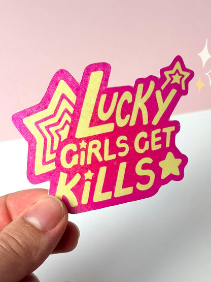 Die-cut holographic vinyl sticker with the text "Lucky Girls Get Kills" in yellow bubble letters with stars on a glittery pink background, held between fingers against a pale background.