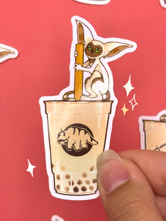 Die-cut vinyl sticker of Momo the lemur from Avatar The Last Airbender perched on a cup of brown sugar bubble tea holding the straw, with an Appa logo on the cup, held between fingers against a coral background.