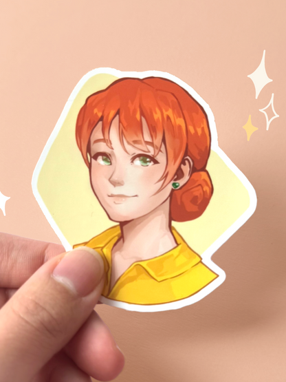 Die-cut vinyl sticker of Penny from Stardew Valley, with red hair in a low bun, green eyes and earrings, wearing a bright yellow collared top, smiling softly on a pale yellow background, held between fingers against a peach background.