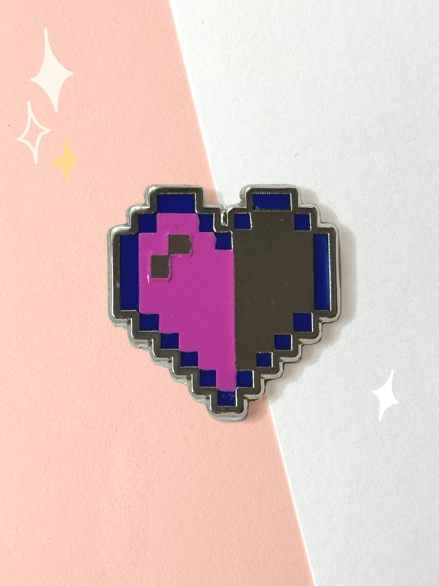 Pixel-art heart hard enamel pin, half magenta with a shine pixel and half mirror chrome, outlined in dark-blue 8-bit pixels on a pink and white background.