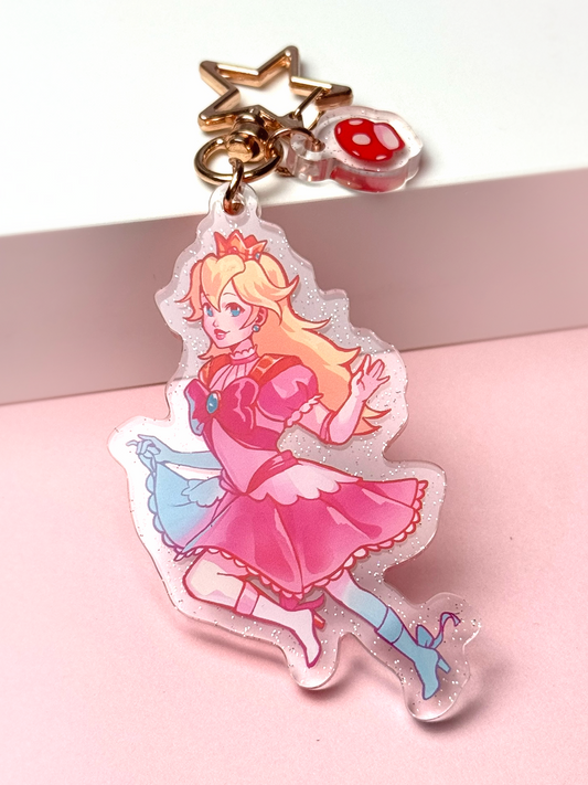 Glitter acrylic keychain of Princess Peach from Super Mario in her pink dress, holding her skirt mid-step, with a star-shaped clasp and a small mushroom charm.