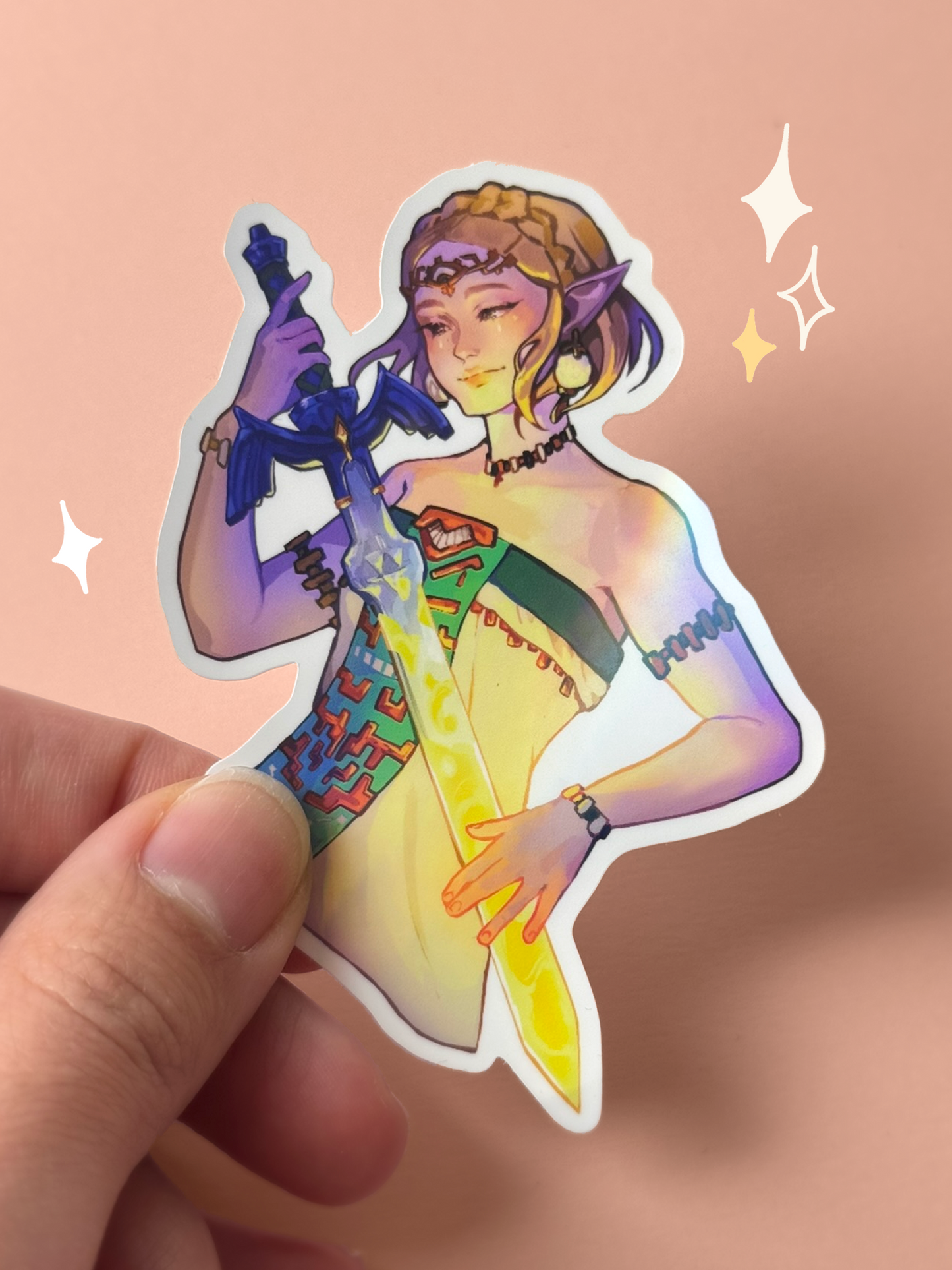 Die-cut holographic vinyl sticker of Princess Zelda from The Legend of Zelda: Tears of the Kingdom, with short braided blonde hair in a white dress with geometric Zonai patterns, holding the Master Sword, held between fingers against a peach background.