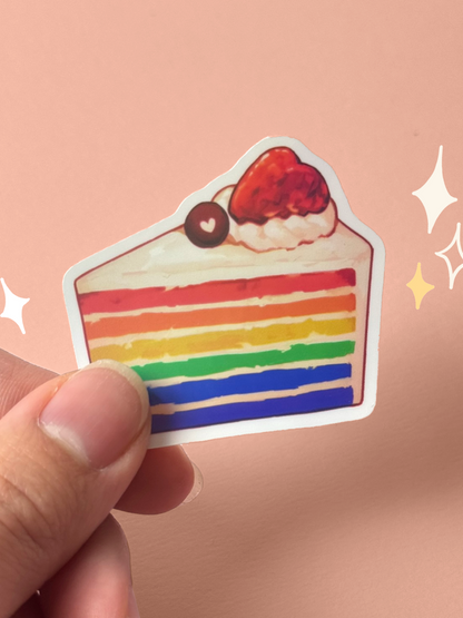 Die-cut holographic vinyl sticker of a slice of rainbow layer cake with red, orange, yellow, green, and blue sponge layers, topped with whipped cream and a strawberry, held between fingers against a peach background.