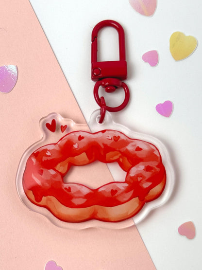 Acrylic keychain shaped like a strawberry-glazed mochi donut with the bubbly pon-de-ring shape and little heart sprinkles, with a red clasp, on a pink and white background with heart confetti.