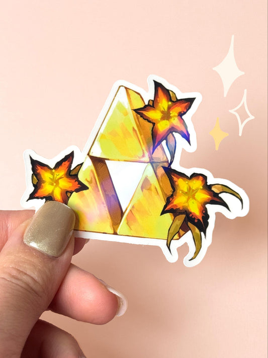 Die-cut holographic vinyl sticker of the golden Triforce from The Legend of Zelda, surrounded by three glowing orange Sundelion flowers, held between fingers against a peach background.