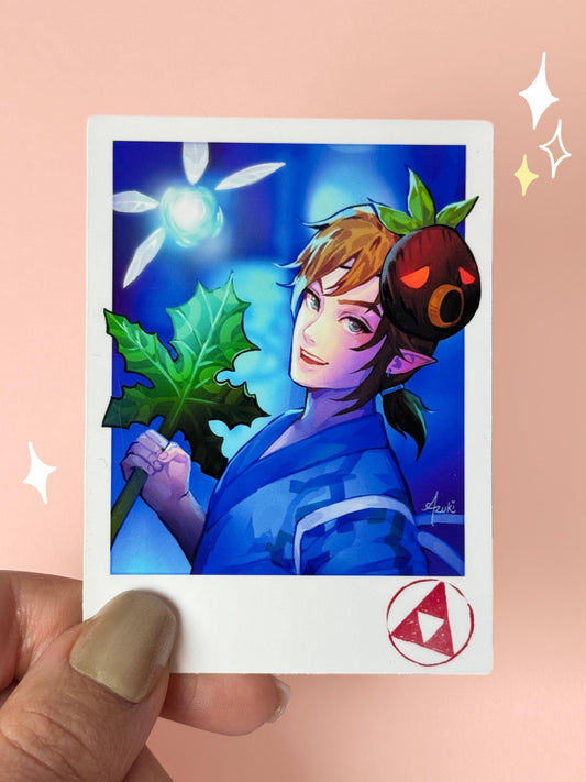 Polaroid-style vinyl sticker of Link from The Legend of Zelda in a blue yukata at a matsuri, holding a Korok leaf, with a Deku mask on his head, a glowing fairy beside him, and a Triforce stamp in the corner, held between fingers against a peach background.