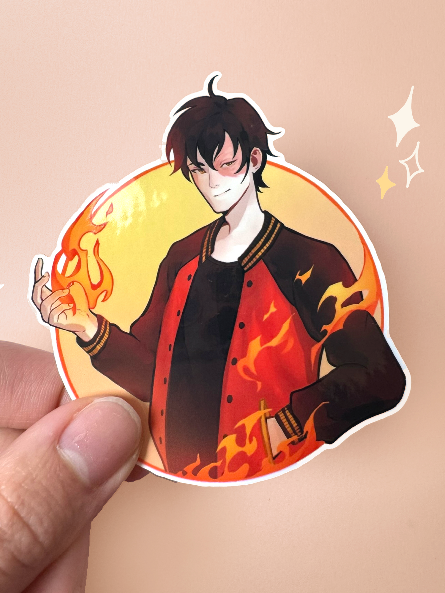 Die-cut vinyl sticker of Zuko from Avatar: The Last Airbender in a modern outfit — black varsity jacket with red and gold flame detailing, his iconic scar over his left eye, with firebending flames swirling around him in a circular yellow frame, held between fingers against a peach background.